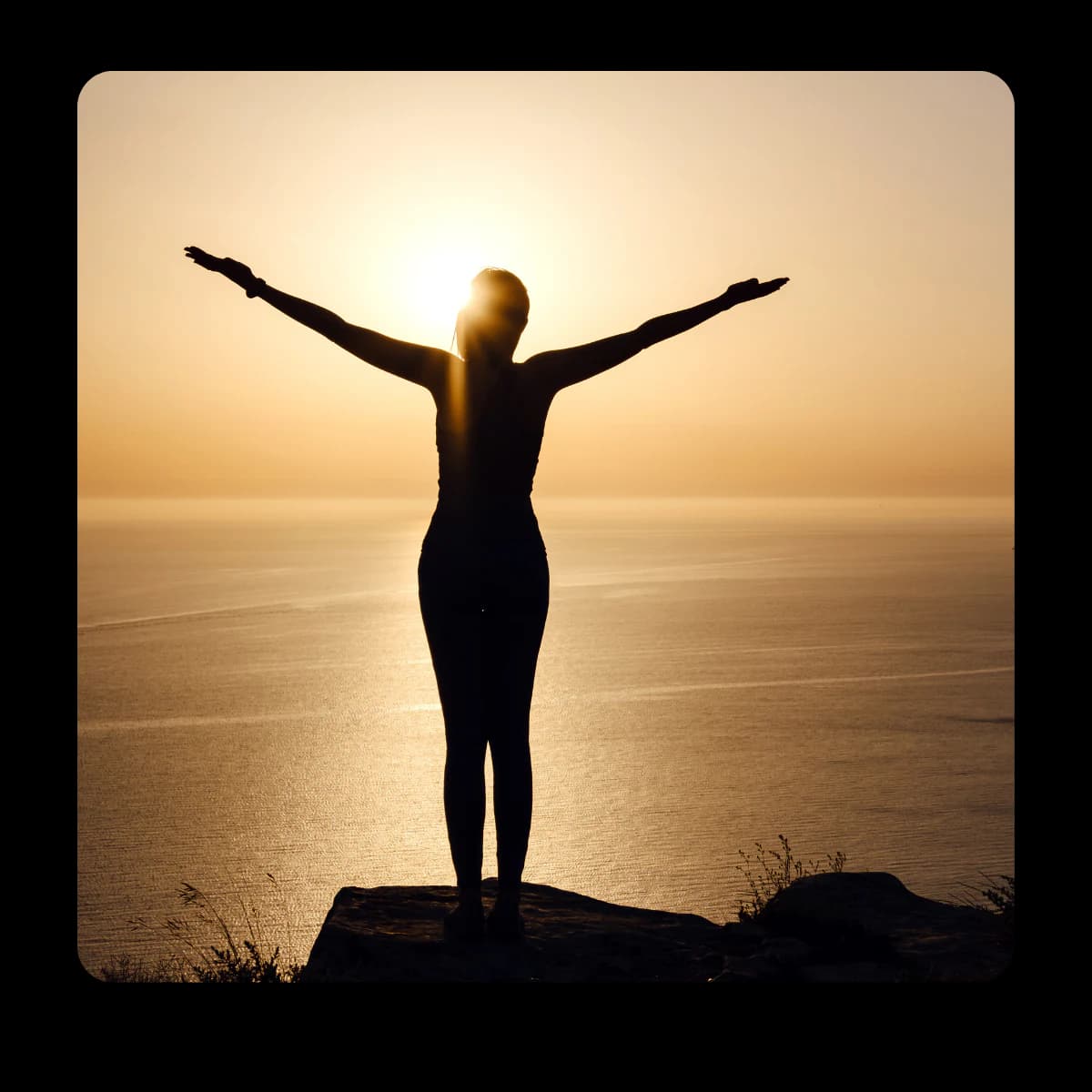 Person with arms raised at sunset overlooking the sea