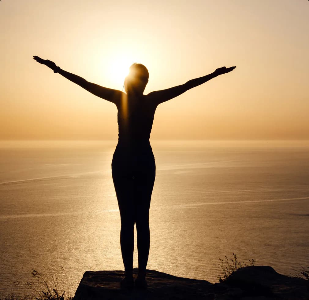 Person with arms raised at sunset overlooking the sea